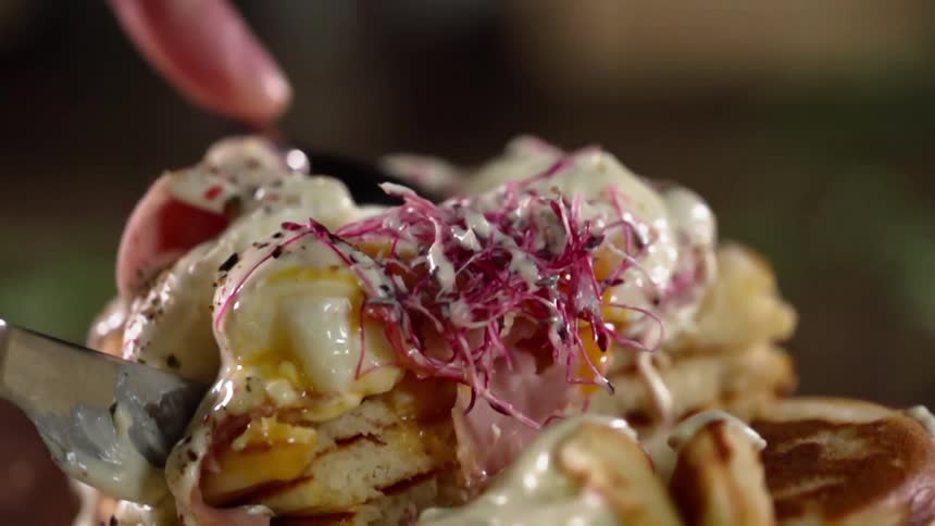 A person cutting in to an egg on top of pancakes