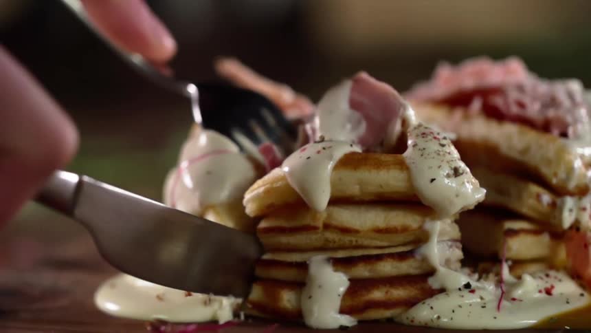 A person uses a knife and fork to cut through pancakes