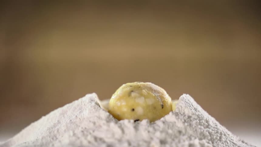 Ball of dough drops onto pile of flour spraying flour about