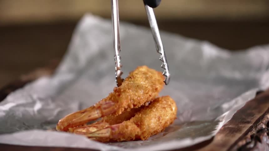 Fried shrimp being plated with tongs onto a piece of parchment paper