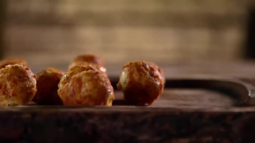 A hand in a black glove tosses some bread food bits on a wooden platter