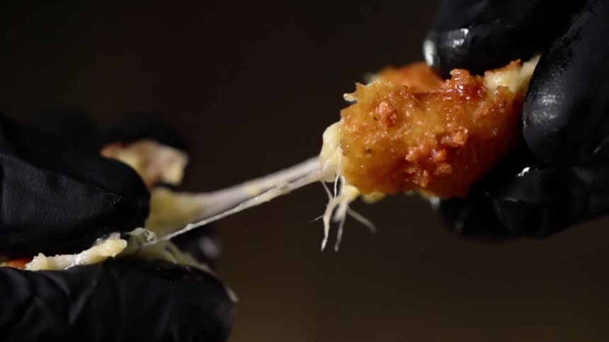 A person wearing gloves pulls a breaded cheesy ball apart