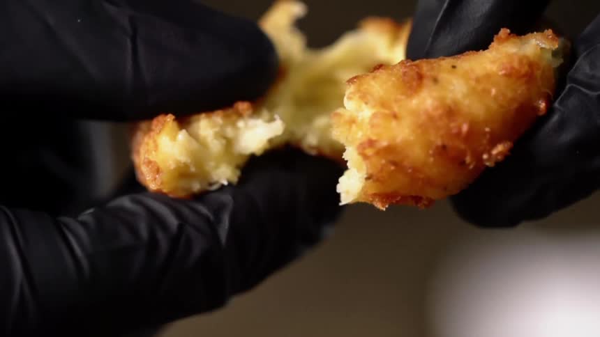 A person wearing black disposable gloves pulls apart a patty covered in breadcrumbs