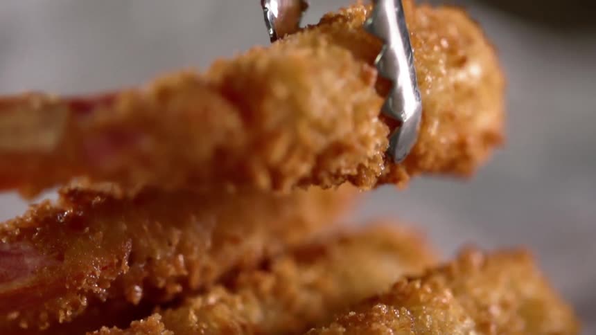 Fried prawns being stacked on a plate with a pair of tongs