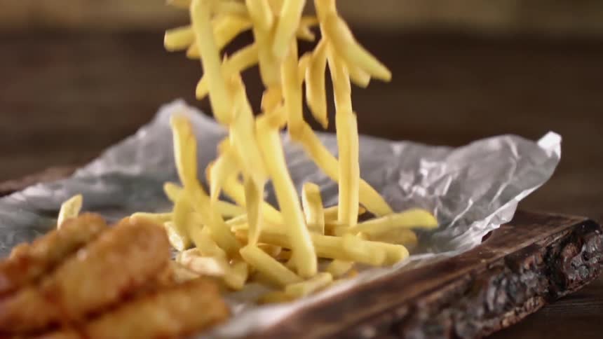 A pile of french fries is dropped on to a piece of paper with fried meat