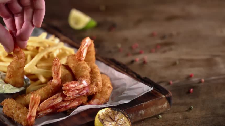 A person dipping fried shrimp in sauce with fries next to it with limes on the table in the background