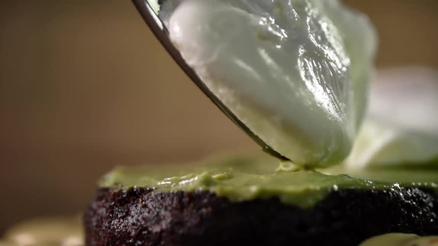A spoon slides a cooked egg on top of a hamburger patty