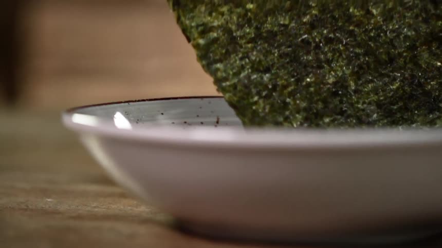 Sheet of dried seaweed falls bouncing into a ceramic white bowl