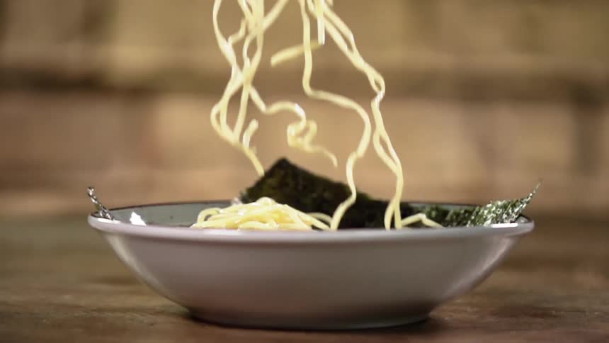 Noodles drop onto seaweed sheet in bowl on wooden surface