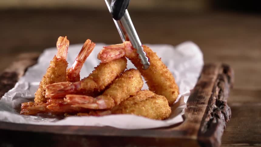 Metal tongs lower a piece of breaded shrimp onto a pile of food