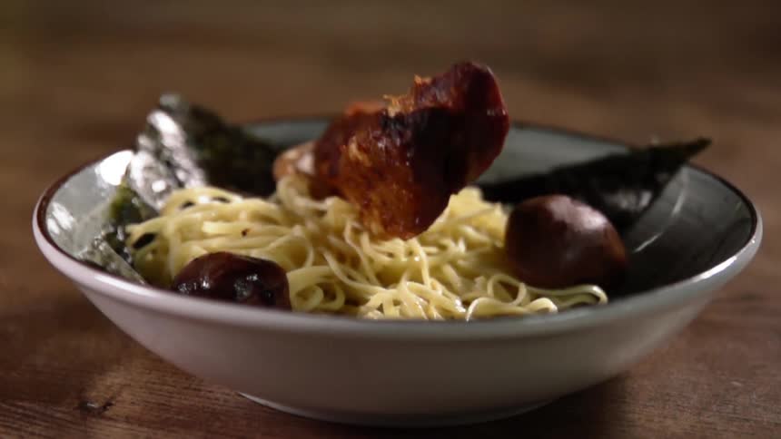 Sliced pork belly bounces as its placed in a bowl of noodles