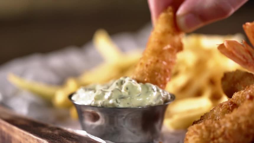 A fried tempura shrimp dipped in white creamy sauce next to french fries