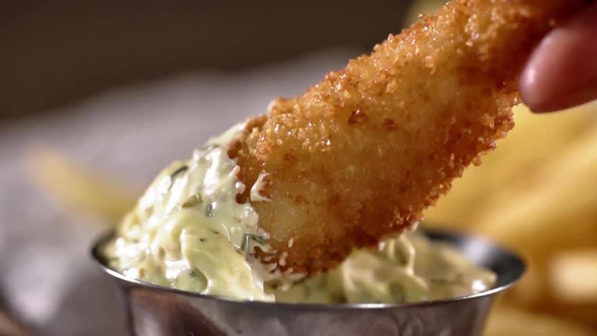 A person dips a fried shrimp in tartar sauce