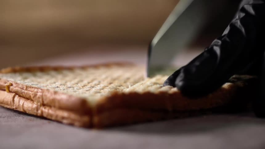 Close up of hands wearing black gloves cutting a toasted sandwich in half