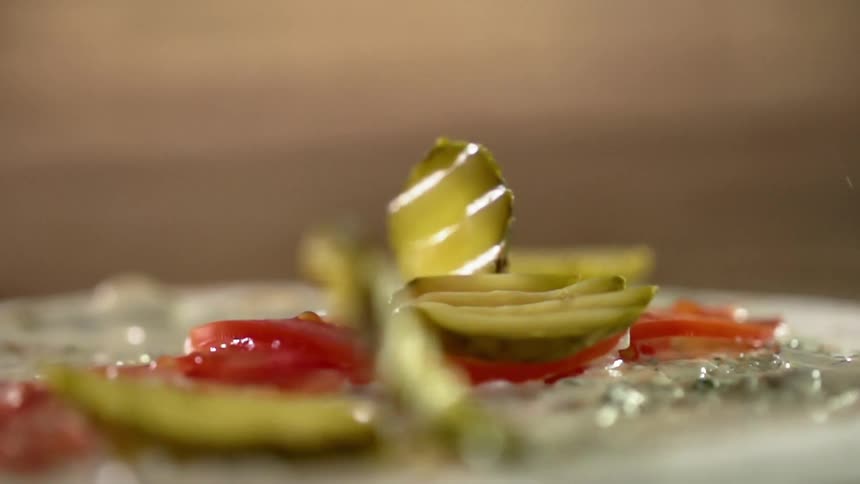 Several pieces of cut pickle are dropped onto a stack of thinly sliced tomatoes