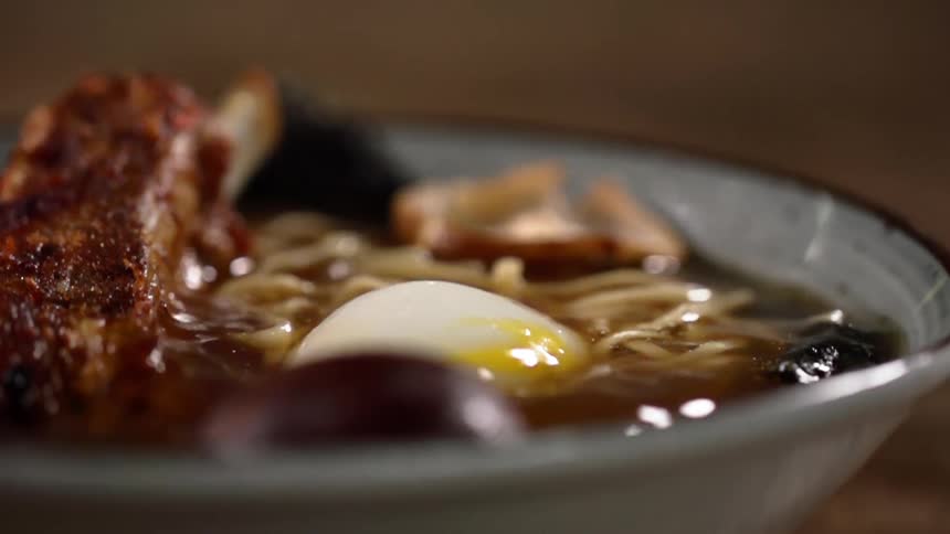 Half of a hard boiled egg is dropped into a bowl of soup made with meat and noodles