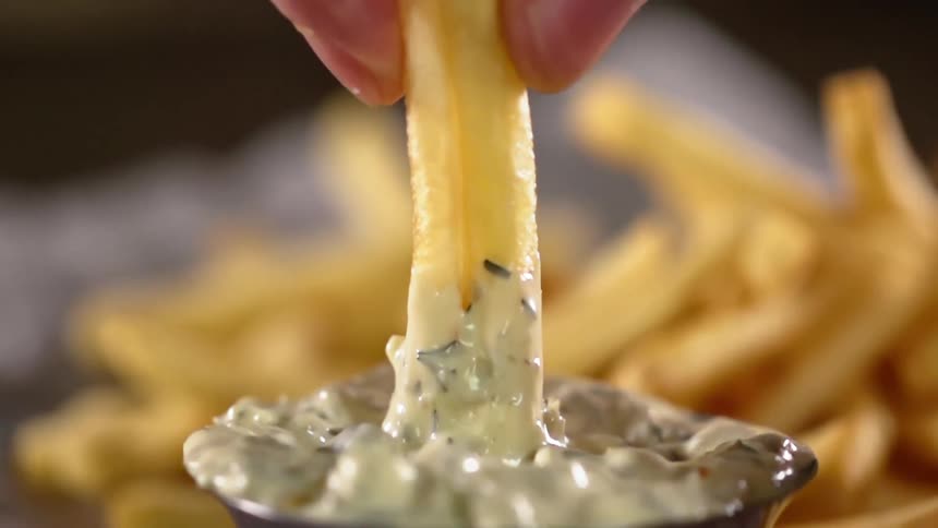 A person dipping a french fry in to sauce
