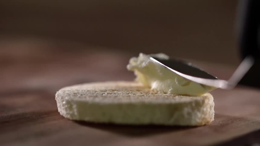 A gloved hand spreads softened butter onto round bread with a butter knife