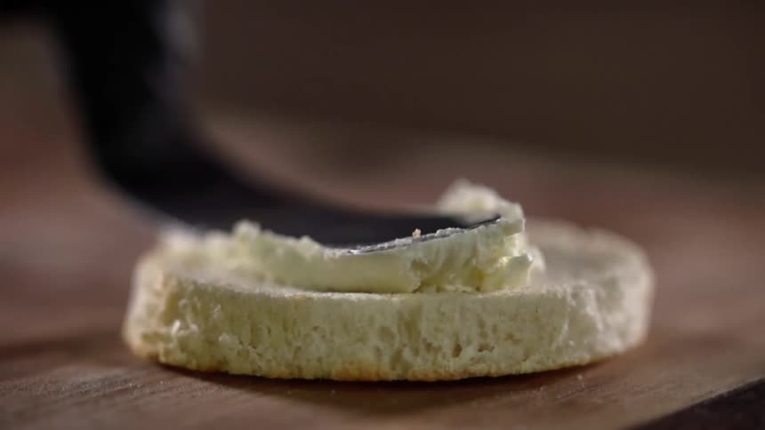 A utensil spreads butter on a piece of bread