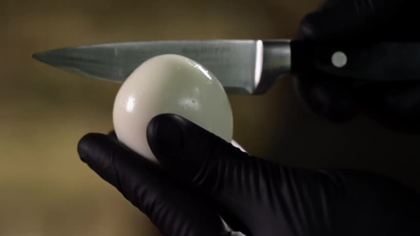 A person wearing black gloves cuts into a hard boiled egg with a knife