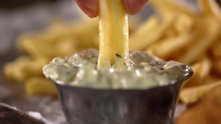 Close up dipping a french fry in tartar sauce