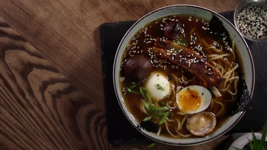 Green vegetables fall into a bowl filled with udon noodle soup