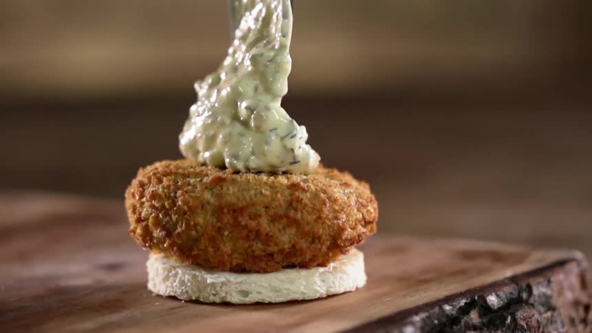 A breaded fish patty receives a generous dollop of tartar sauce