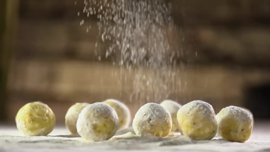 Grains of sugar fall onto balls of dough lying on a tabletop