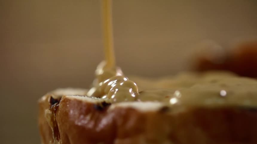 A sliced bread bun has a thick brown sauce drizzled onto its open surface
