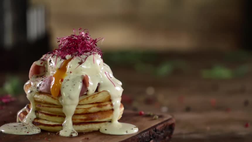 Pancakes on a wooden platter on a table with cream and egg yolk dripping off of it