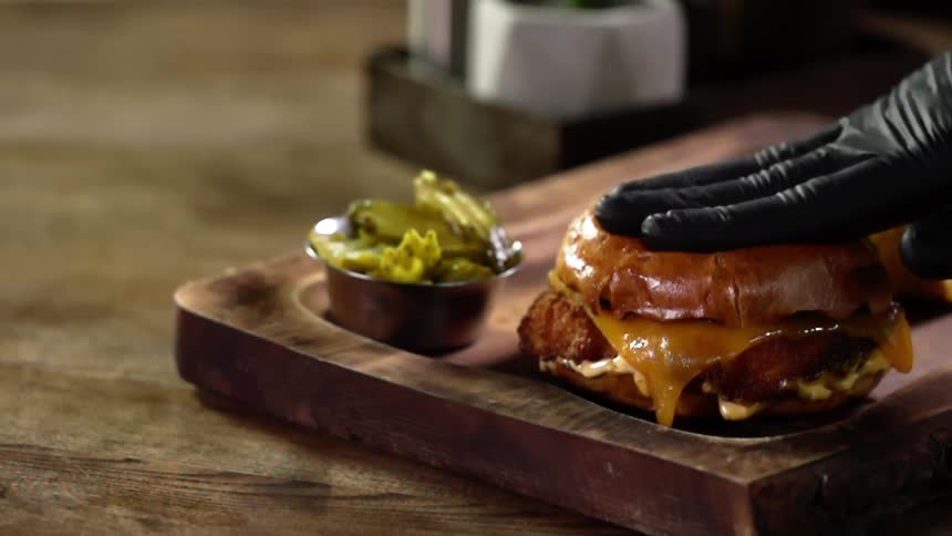 A hand in a black glove pushes down on a hamburger bun