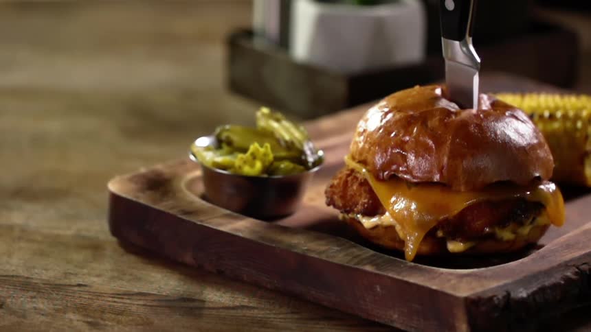 Sharp kitchen knife cuts a gourmet cheese burger on a wooden board