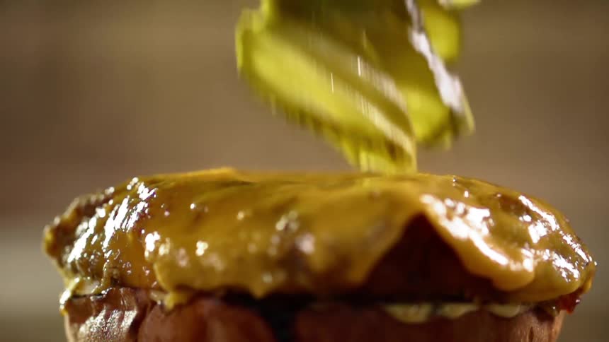 Pickles falling onto a cheeseburger patty and bun