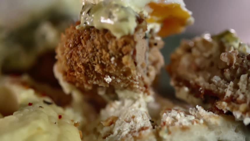 A fork lifts a piece of breaded food covered in tartar sauce