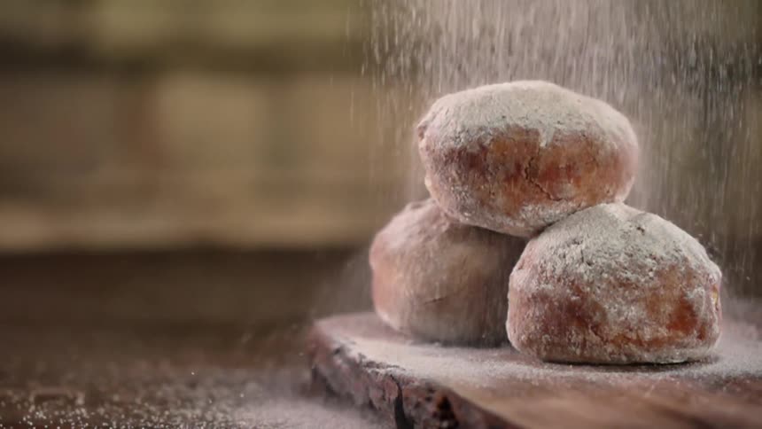 Powdered sugar is sprinkled over baked goods on a wood cutting board