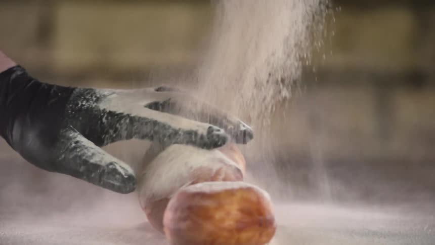 A person wearing a black disposable glove sprinkles flour over a couple of bread pastries
