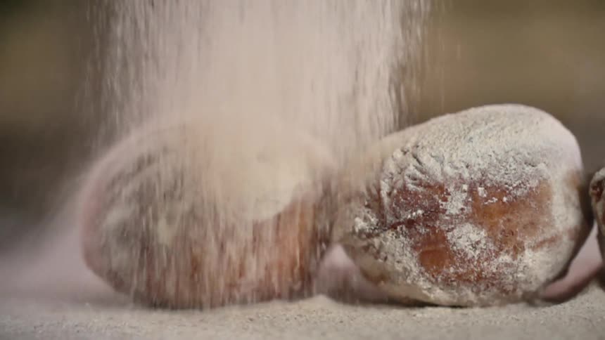 Powdered sugar falls to coat line of donuts