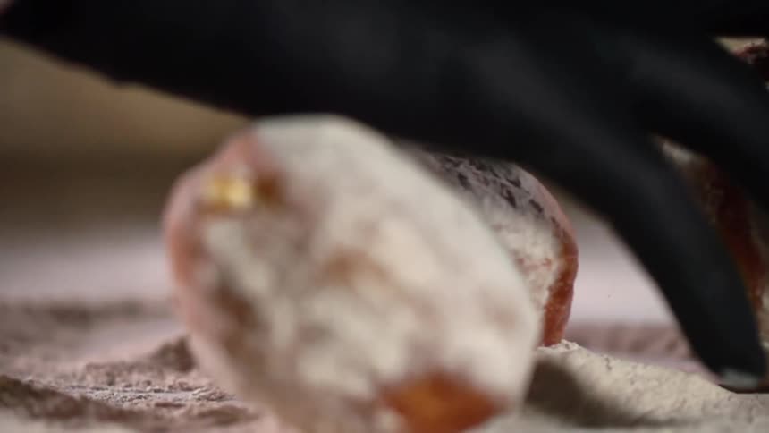 A gloved hand rolls bread around in a pile of flour