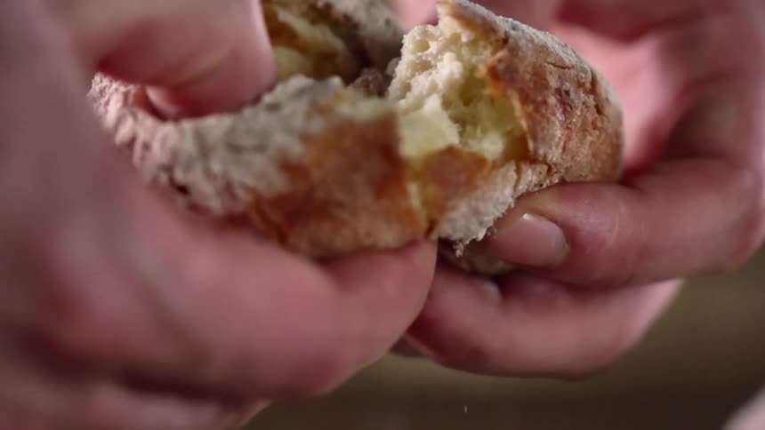 Person breaks bread in half letting crumbs fall