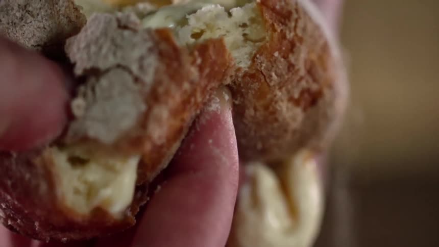 A person squeezes and pulls apart a cream filled bread pastry and the cream oozes out