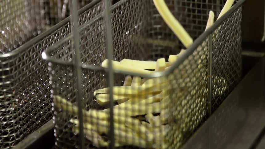 French fries falling into the frying basket of a large fryer