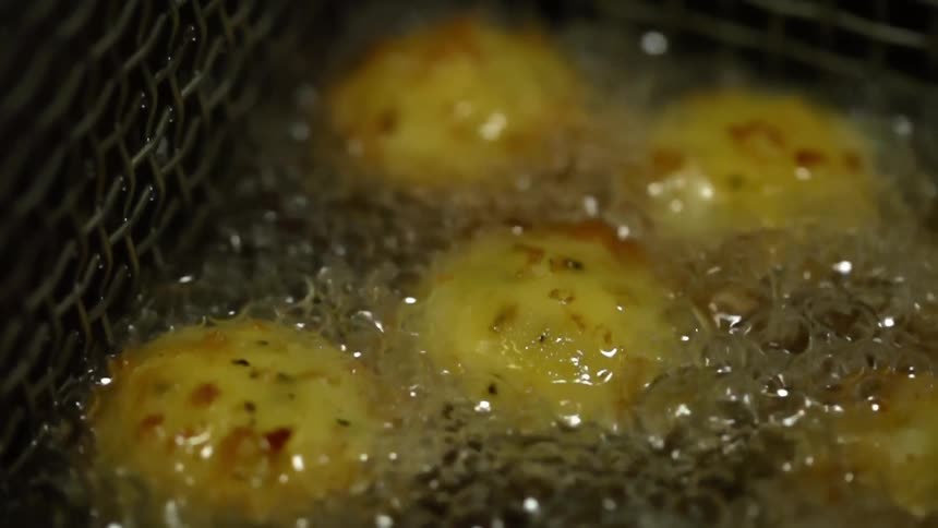 Buns deep frying in hot oil inside metal basket