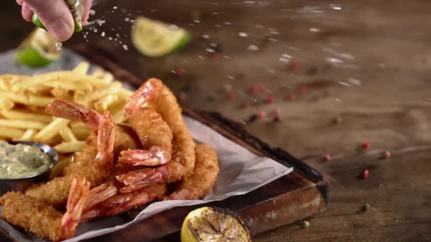 A person squeezes lemon juice over a tray of fried shrimp and french fries