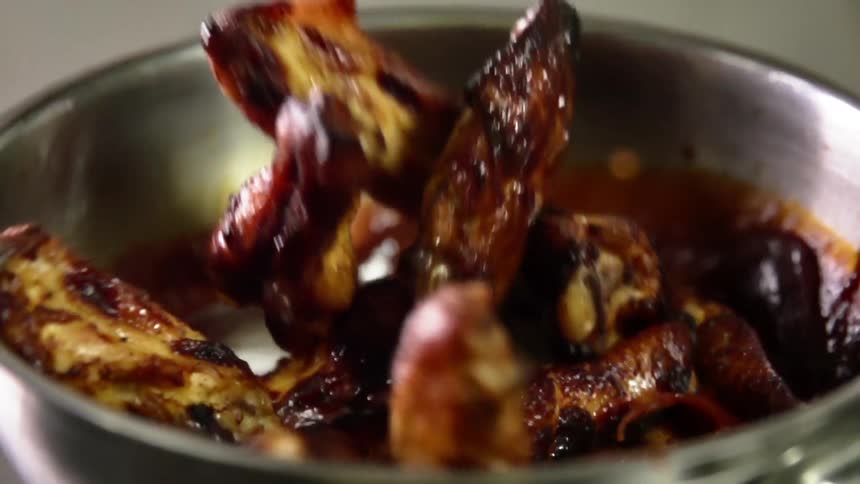 Chicken wings going in to a bowl of sauce