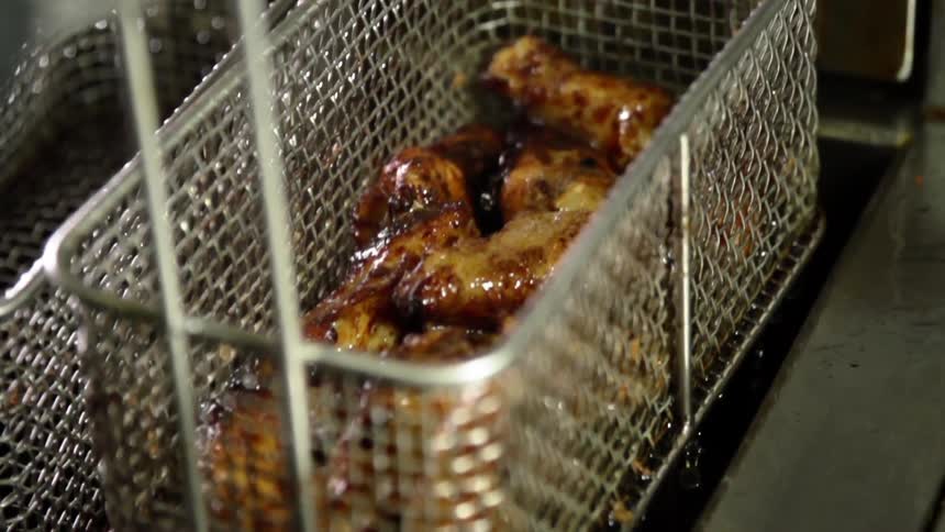 A fryer basket being lifted from the oil of a deep fryer to reveal the fried chicken within