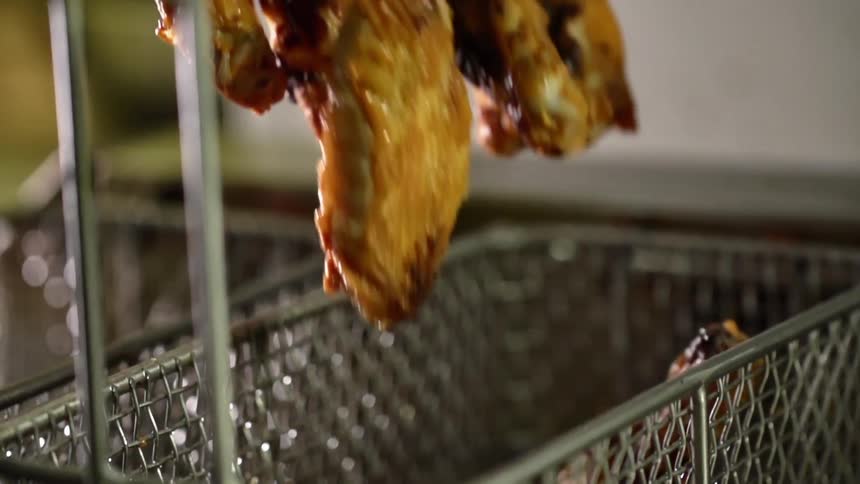 Cooked chicken wings and chicken drummets are poured from a metal bowl into the fryer basket at a restaurant