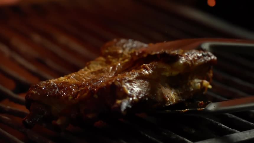 A piece of steak is placed on a grill with tongs