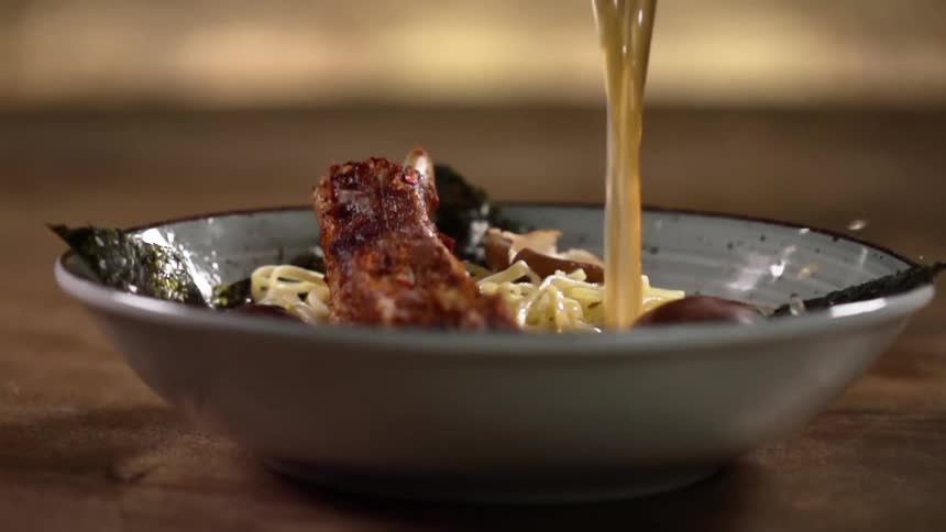 A bowl of noodles and meat has broth poured over it to make a delicious soup