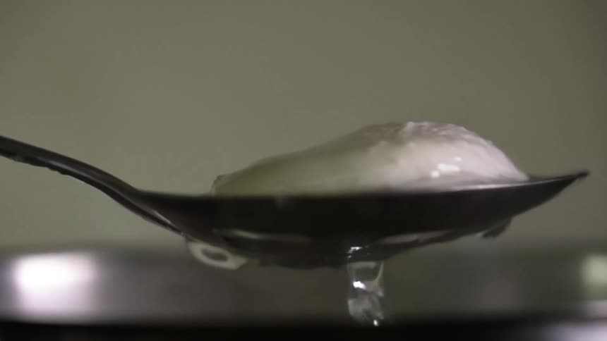 A partially cooked egg is lifted out of water with a spoon