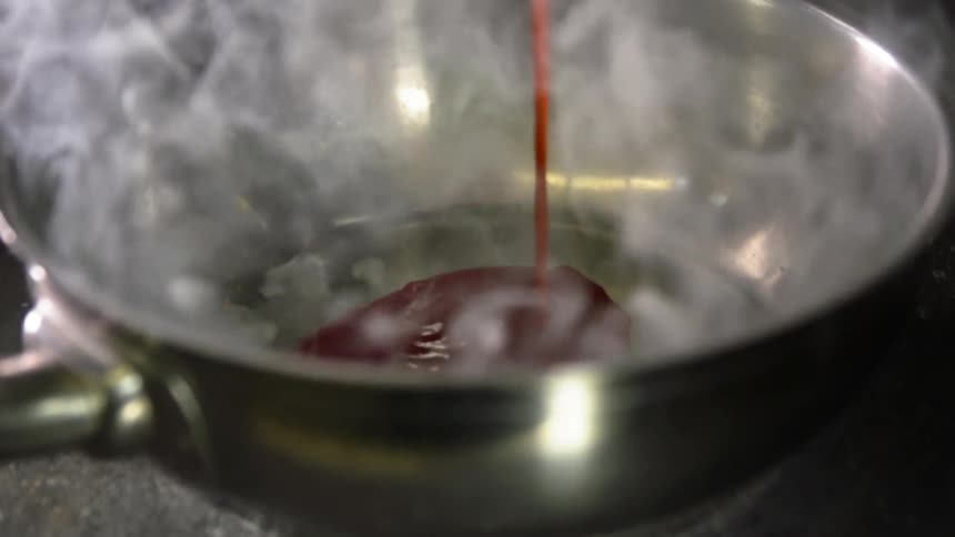 A red sauce pours into a hot pan on a stove